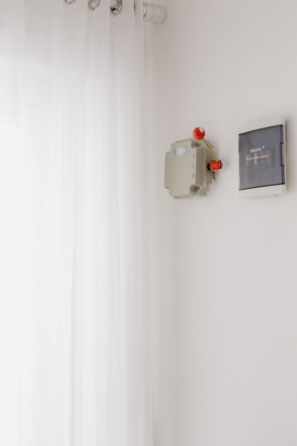 Een schakelaar en een knop op een witte muur naast een gordijn
