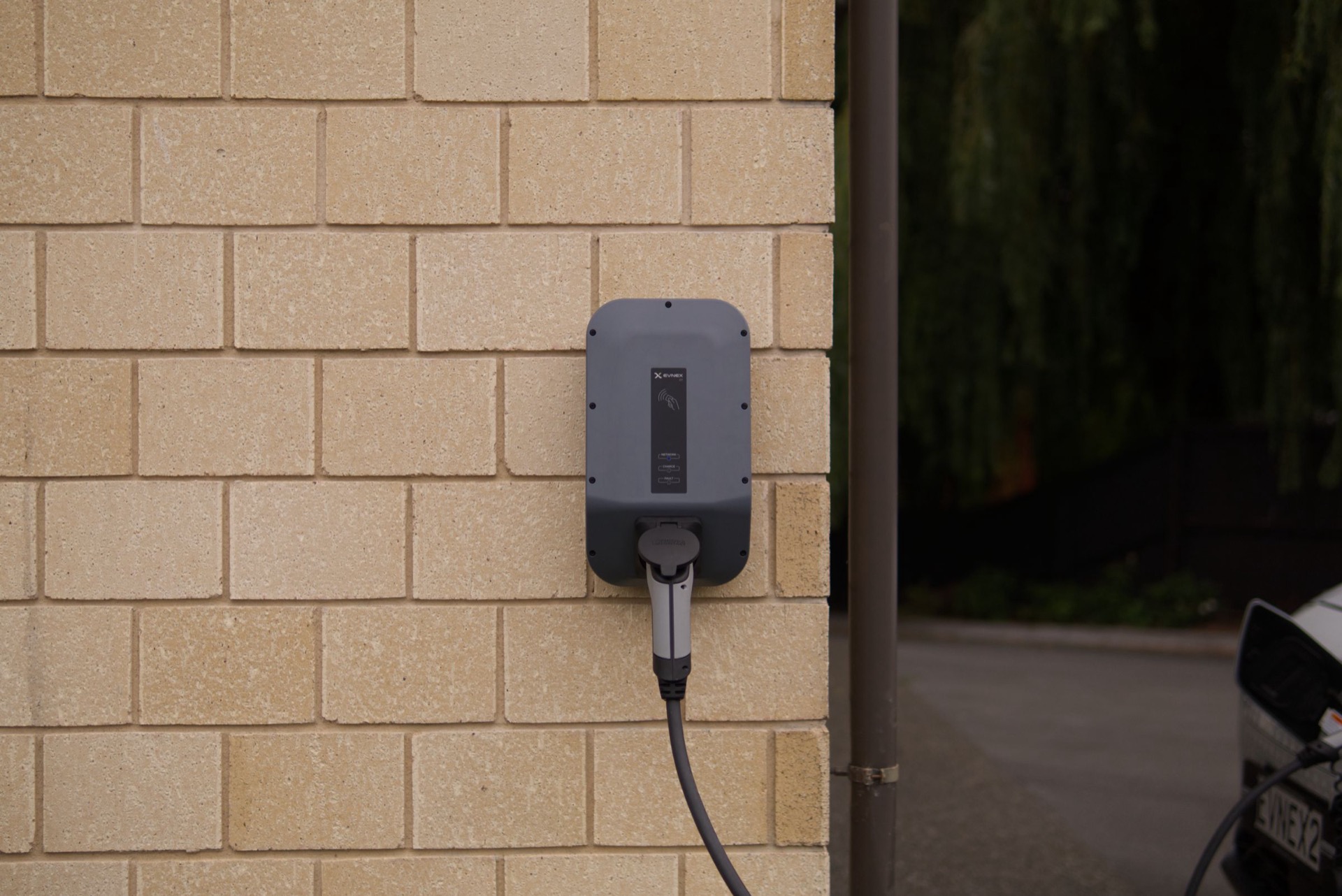 Een grijze laadpaal aan een bakstenen gevel met een kabel eronder
