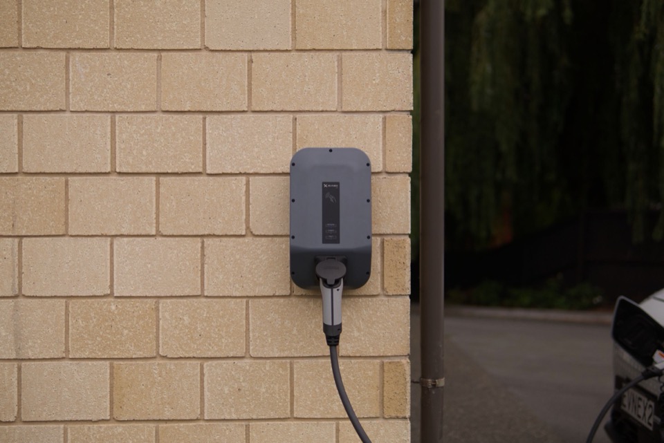 Een grijze laadpaal aan een bakstenen gevel met een kabel eronder
