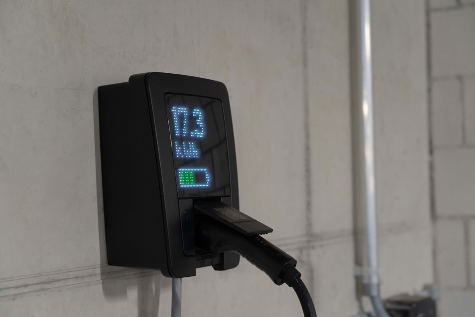 Een zwarte laadpaal met een display dat 17,3 kWh toont aan een lichte muur